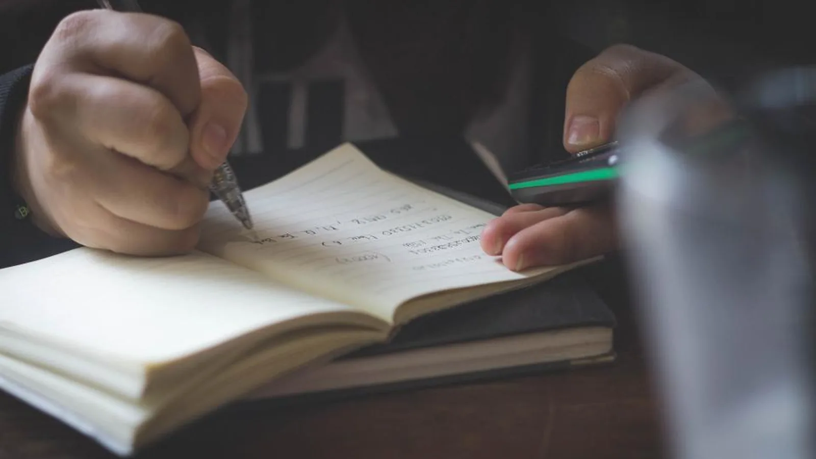 Mão escrevendo anotações num caderno aberto
