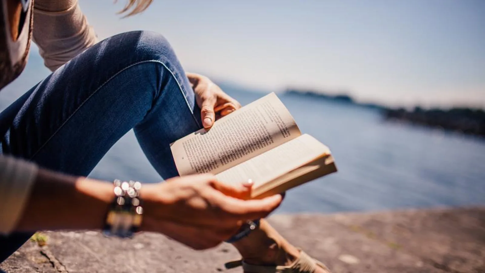 Pessoa lendo um livro sentada ao ar livre, perto da água