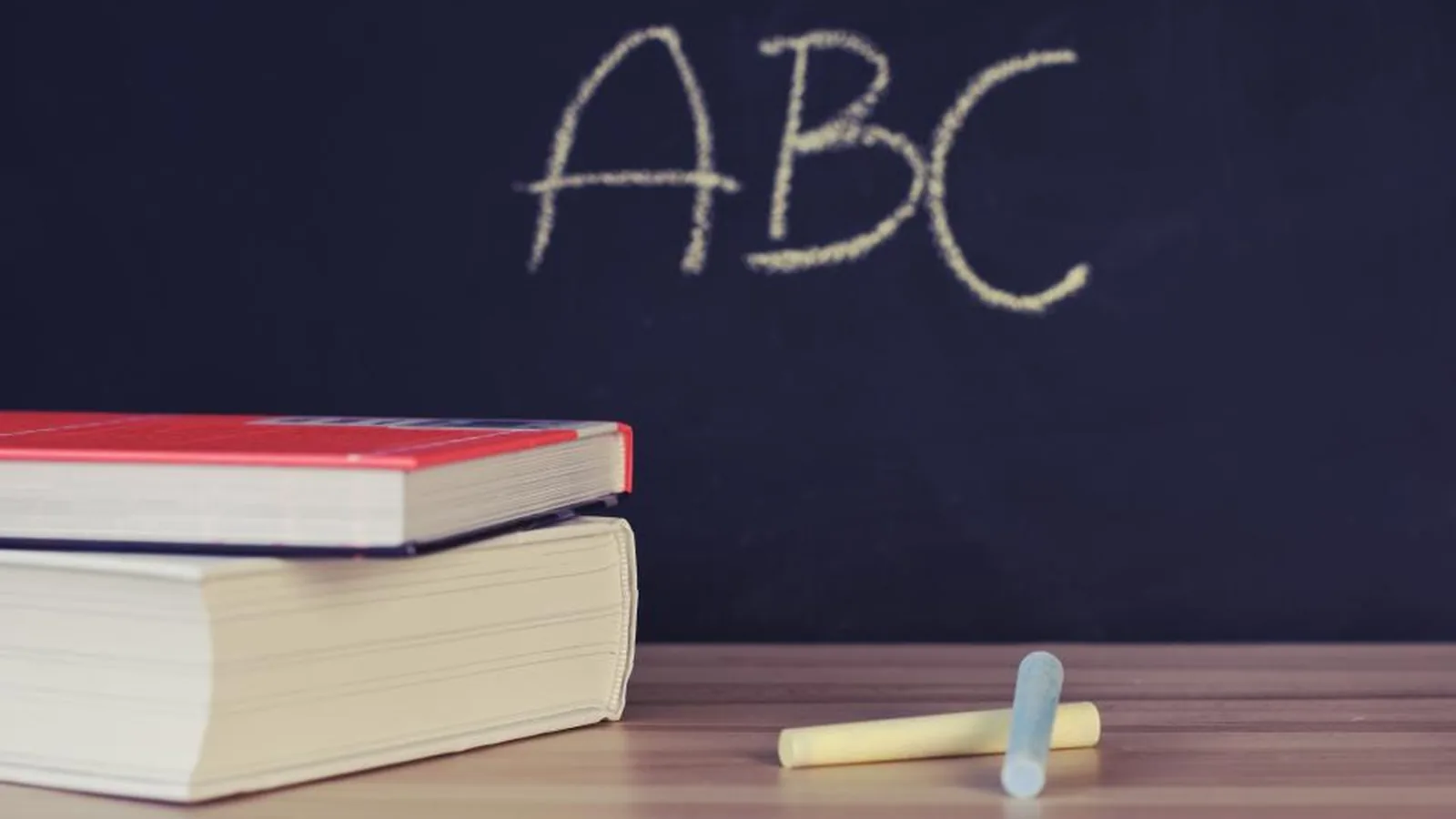 Quadro-negro escrito ABC, com livros empilhados e giz na mesa